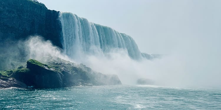 Giant American Falls waterfall causing cloudy mist over beautiful water and green-covered rocks at Niagara Falls.
