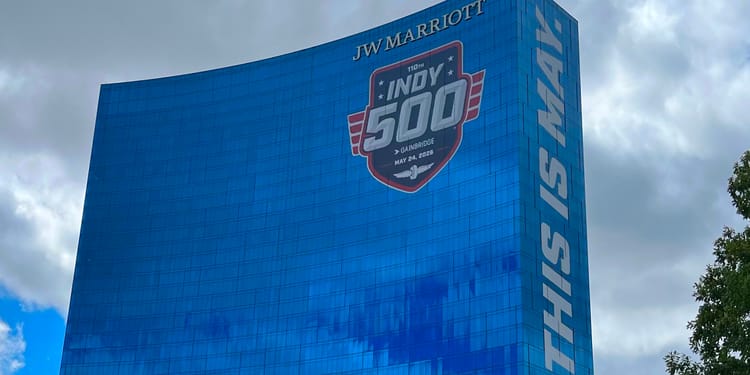 Indy 500 banner plastered onto a titanic Marriott hotel, 100% mirrored windows reflecting the sky.