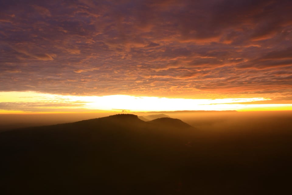 Golden sunrise between heavy clouds and dark hilltops.
